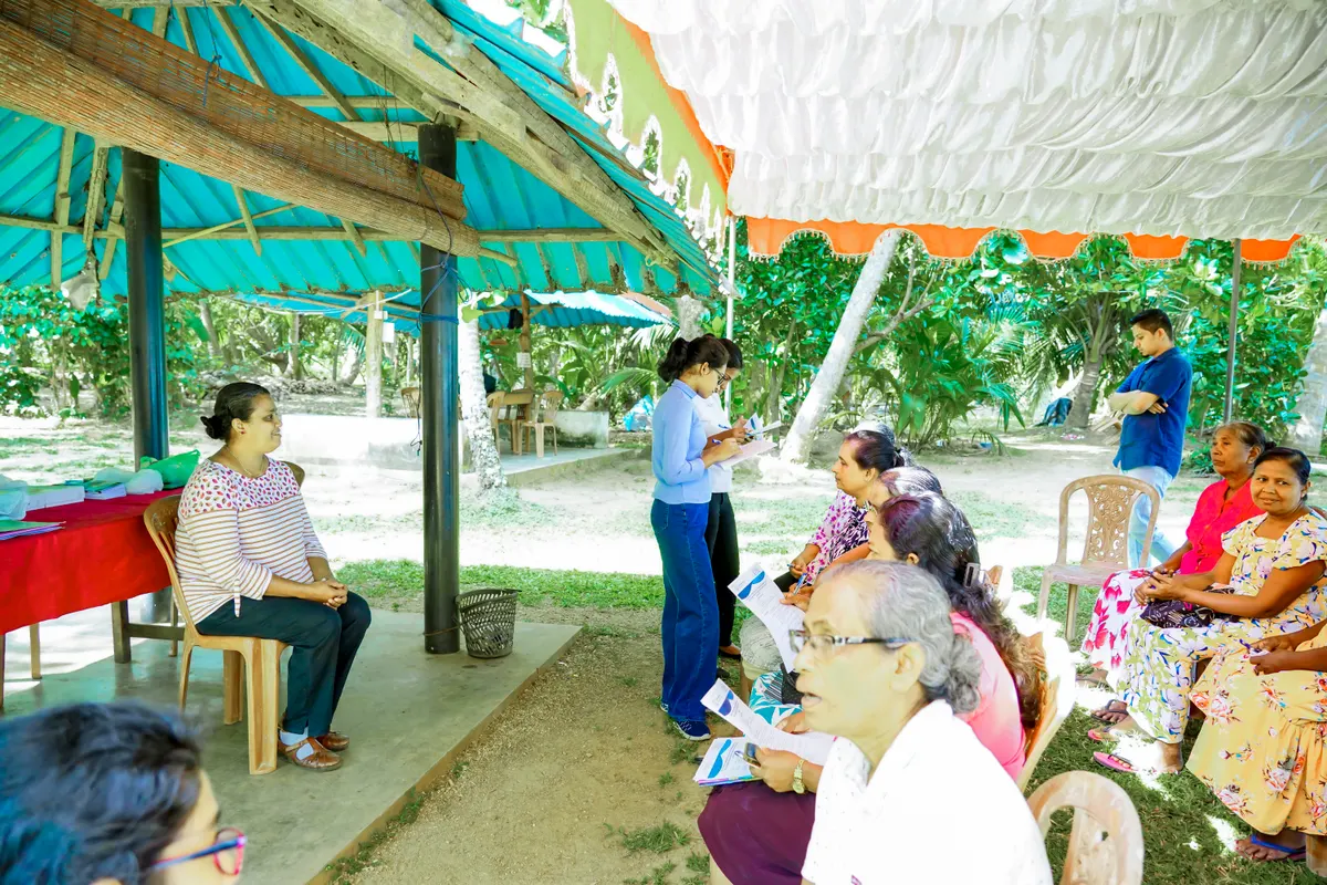 A facilitator speaking with women fish processors seated under a canopy